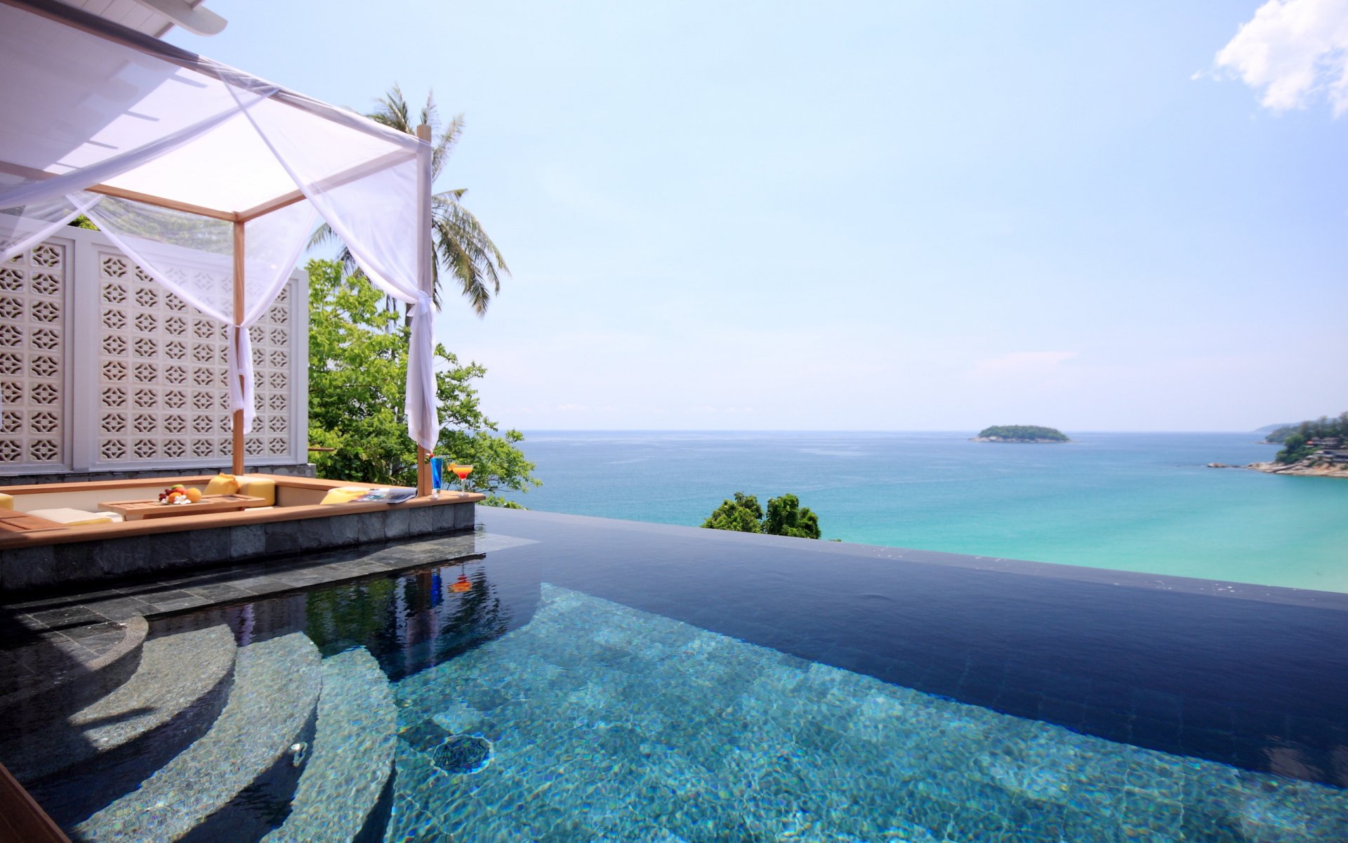 2K Quad HD desktop wallpaper: man-made infinity pool overlooking turquoise ocean from a seaside pavilion with canopy, palm trees and distant islets.