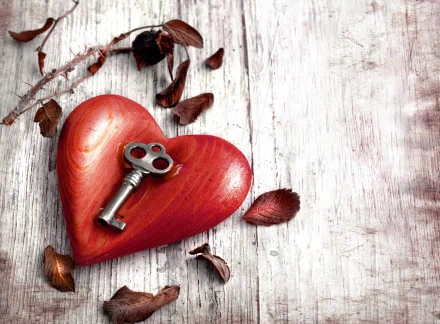 A 4K Ultra HD Valentine's Day desktop wallpaper featuring a red wooden heart with an antique key resting on it, surrounded by dried leaves on a rustic wooden surface.