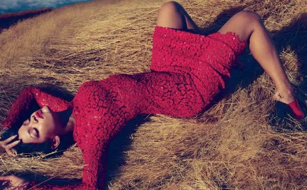 Rihanna in a red dress lying on dry grass, captured in a stylish HD PC desktop wallpaper highlighting her music icon status.