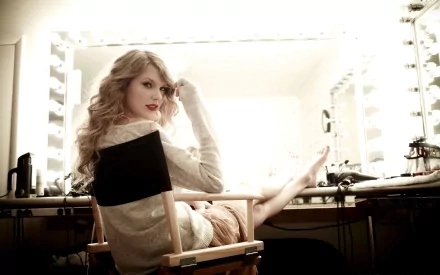 HD desktop wallpaper featuring Taylor Swift seated in a director's chair in a brightly lit dressing room.