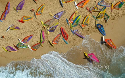 HD PC desktop wallpaper and background: aerial view of colorful windsurfing sails and boards scattered on a sandy beach as waves lap the shore — Sports.