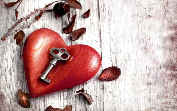A 4K Ultra HD Valentine's Day desktop wallpaper featuring a red wooden heart with an antique key resting on it, surrounded by dried leaves on a rustic wooden surface.