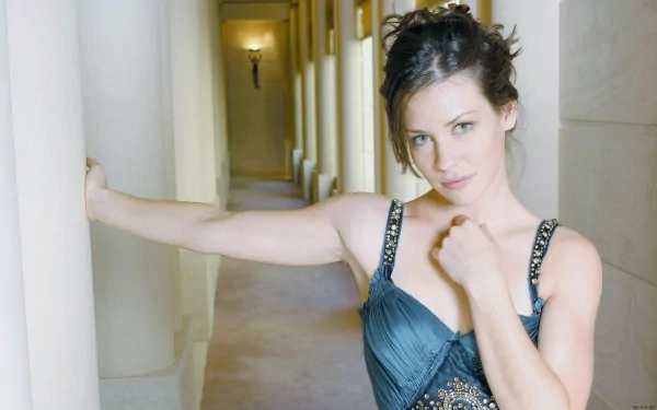 HD PC desktop wallpaper featuring a portrait of celebrity Evangeline Lilly posing confidently in a sleeveless dress along a softly lit hallway.