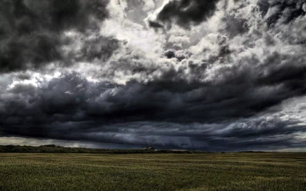 HD PC desktop wallpaper showcasing a dramatic nature scene with dark, stormy clouds looming over a vast open field under an intense sky.