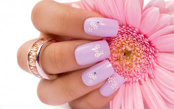 Close-up of a woman's hand with lilac nail art and rings holding a pink gerbera daisy — 2K Quad HD PC desktop wallpaper/background.