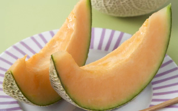 Fresh melon slices displayed on a striped plate, showcasing their juicy, orange flesh against a soft green background. An appetizing food-themed HD desktop wallpaper.