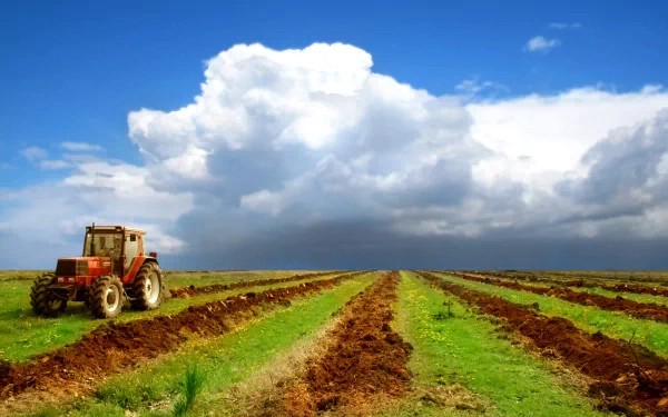 A vibrant 4K Ultra HD image of a tractor positioned beside freshly plowed fields under a bright blue sky with fluffy clouds, showcasing the beauty of agricultural landscapes.
