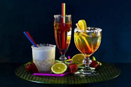 4K Ultra HD wallpaper featuring three vibrant cocktails garnished with lemon and strawberries, set against a dark background on a woven surface.