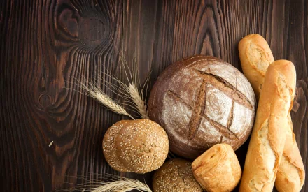 2K Quad HD PC desktop wallpaper and background showing assorted bread loaves and wheat on a dark wooden table — food, bread.