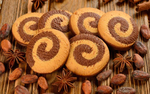 HD desktop wallpaper featuring swirled chocolate and vanilla cookies arranged with star anise and cocoa beans on a wooden surface.