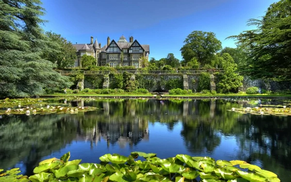 A stunning HD wallpaper featuring a majestic man-made castle surrounded by lush greenery and serene waters, reflecting the vibrant blue sky above and lily pads in the foreground.