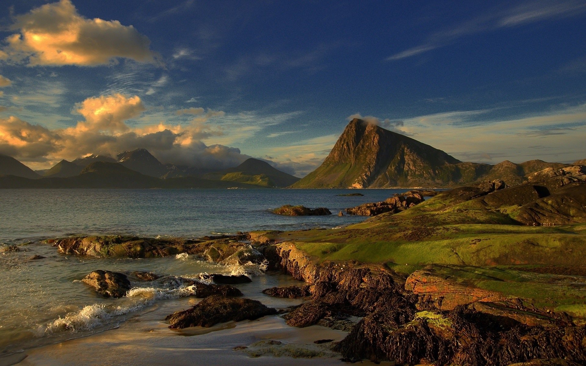 HD desktop wallpaper showcasing a serene lake surrounded by rocky shores and mountains under a vibrant sky with clouds, capturing the beauty of nature.