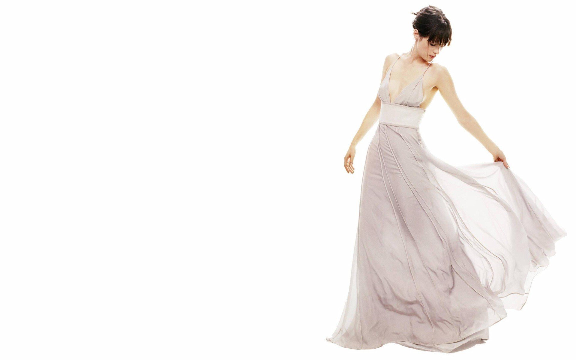 A high-definition desktop wallpaper featuring Zooey Deschanel, elegantly dressed in a flowing, light-colored gown, captured in a graceful pose against a clean, white background.