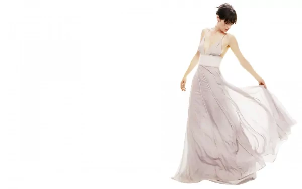 A high-definition desktop wallpaper featuring Zooey Deschanel, elegantly dressed in a flowing, light-colored gown, captured in a graceful pose against a clean, white background.