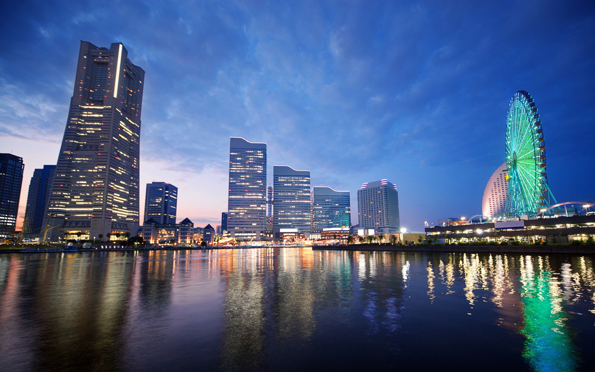 A stunning night view of Yokohama, Japan, featuring a vibrant Ferris wheel and illuminated buildings reflected in the water, showcasing the city's man-made beauty.