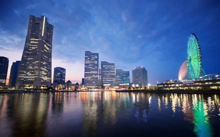 A stunning night view of Yokohama, Japan, featuring a vibrant Ferris wheel and illuminated buildings reflected in the water, showcasing the city's man-made beauty.