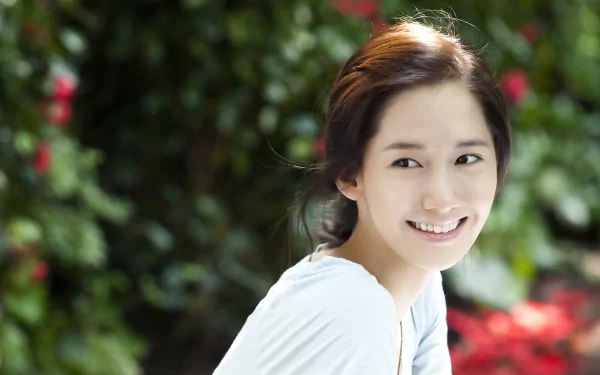 A smiling Im Yoona is featured against a lush green background, showcasing her connection to nature and music, creating a vibrant HD desktop wallpaper for fans of Innisfree.