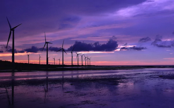 HD desktop wallpaper featuring a row of man-made wind turbines silhouetted against a vibrant purple and orange sunset sky over reflective water.