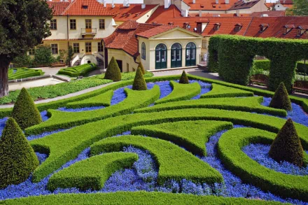 HD desktop wallpaper featuring Prague Botanical Garden in the Czech Republic, showcasing manicured hedges and vibrant flower beds against charming historic buildings.