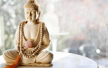 HD wallpaper featuring a serene Buddha statue adorned with prayer beads in a peaceful setting, evoking elements of Buddhism.