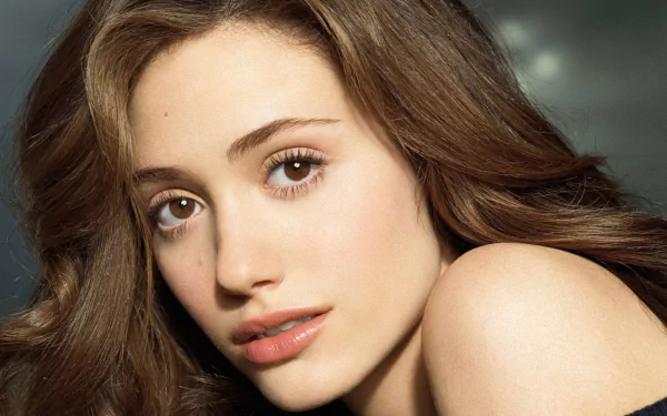 Close-up HD desktop wallpaper of celebrity Emmy Rossum with soft waves in her hair and a neutral expression against a blurred dark background.