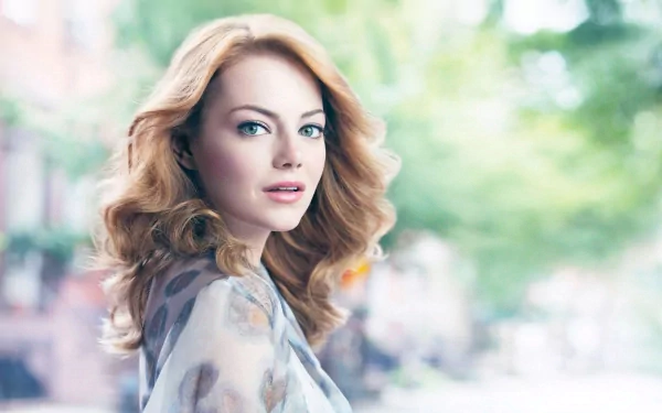 HD desktop wallpaper featuring celebrity Emma Stone with soft-focus trees and buildings in the background.