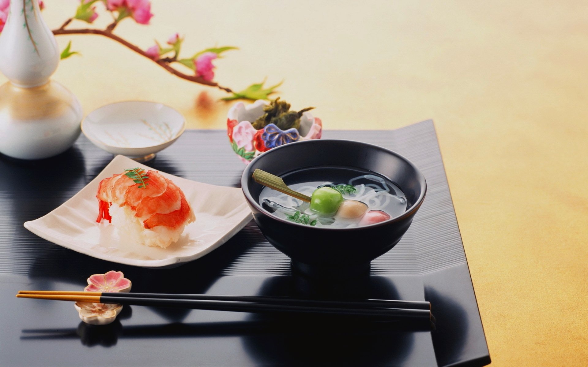 HD PC desktop wallpaper featuring a beautifully arranged sushi plate with chopsticks and a bowl of soup on a black tray, accented by delicate cherry blossoms.