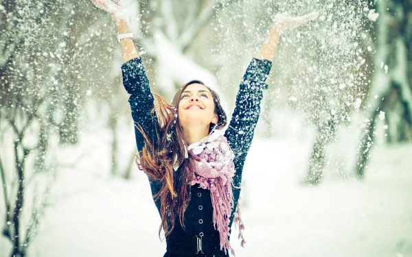 A joyful woman with outstretched arms celebrates in a snowy landscape, capturing a vibrant mood. This HD desktop wallpaper radiates happiness and winter charm.