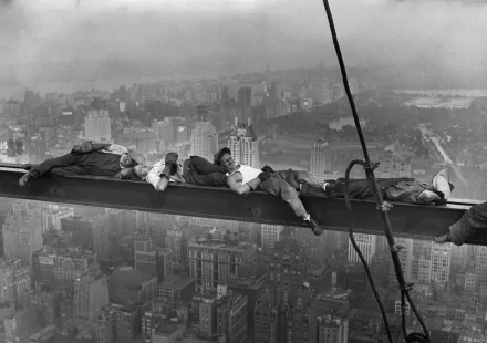 A historic black-and-white image of heavy workers resting on a steel beam high above an urban skyline, showcasing the bravery and resilience of laborers in the early industrial era.