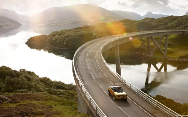 Yellow 2011 Land Rover DC100 Sport concept vehicle crossing a curving coastal bridge at sunset, scenic HD PC desktop wallpaper and background.