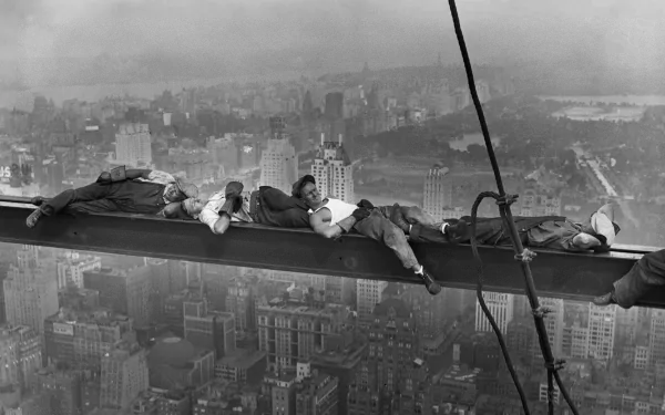 A historic black-and-white image of heavy workers resting on a steel beam high above an urban skyline, showcasing the bravery and resilience of laborers in the early industrial era.