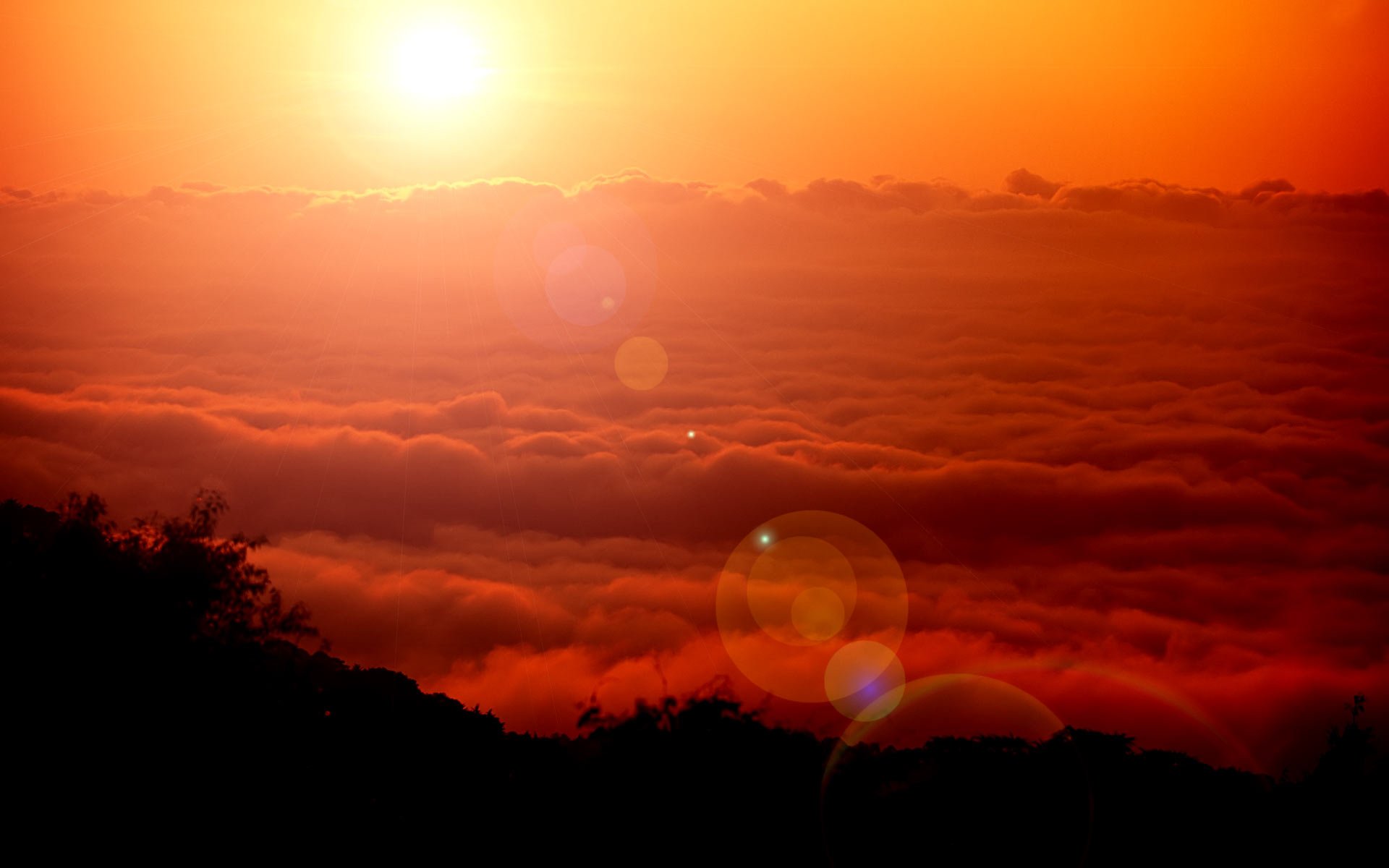 HD fantasy nature desktop wallpaper featuring a vibrant orange sunset above a thick blanket of clouds over a dark silhouetted landscape.