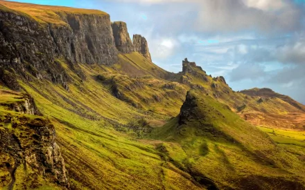 2K Quad HD PC desktop wallpaper and background: nature cliff scene of sweeping green cliffs and rocky spires beneath a brooding cloudy sky.