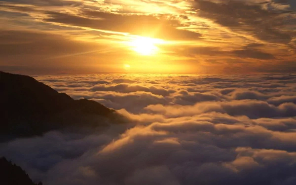 A vibrant HD desktop wallpaper showing a glowing sun setting above a vast sea of clouds over a mountainous horizon.