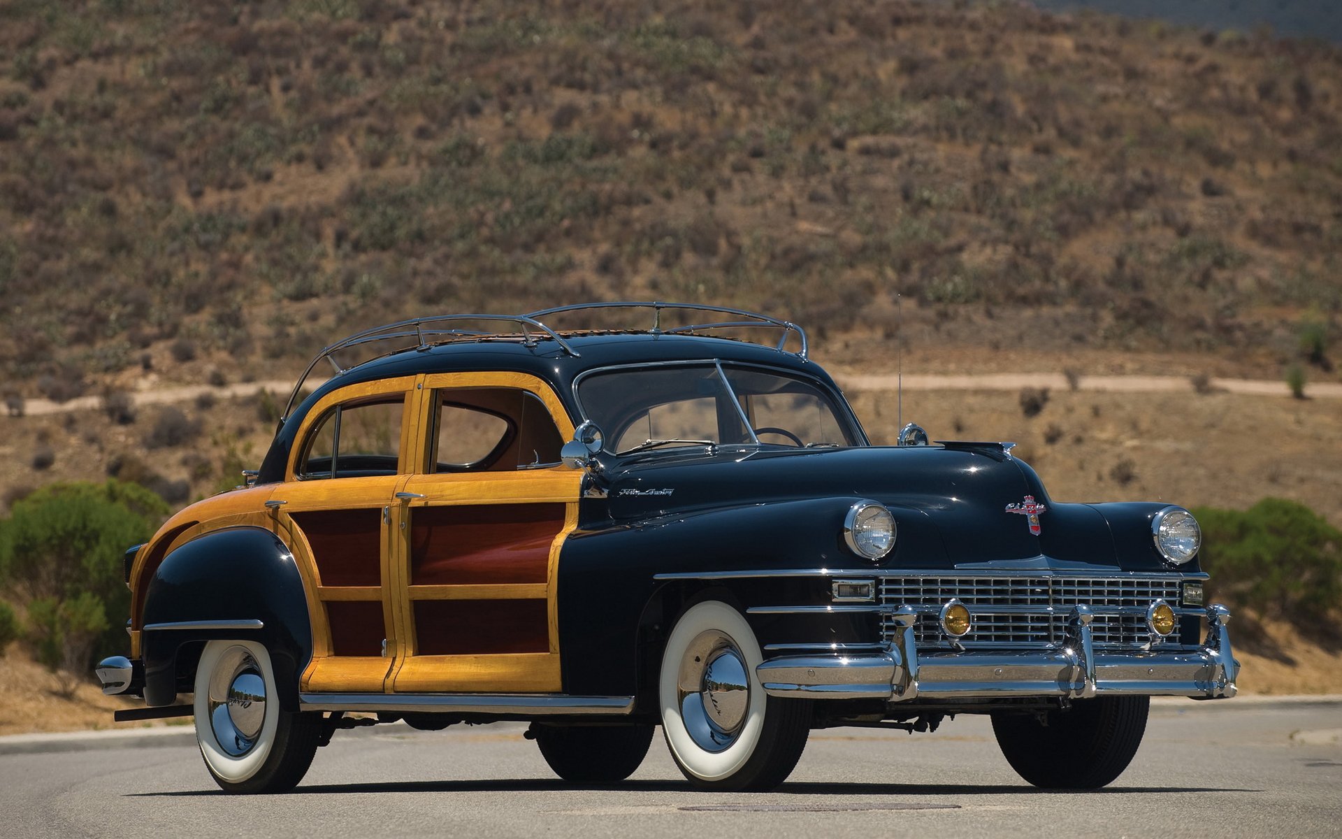 A 1947 Chrysler Town & Country classic vehicle parked on a desert road, showcased in a high-definition PC desktop wallpaper and background.