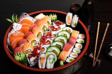 HD desktop wallpaper featuring a vibrant platter of assorted sushi rolls and sashimi, accompanied by chopsticks, soy sauce, and wasabi on a dark wooden table.