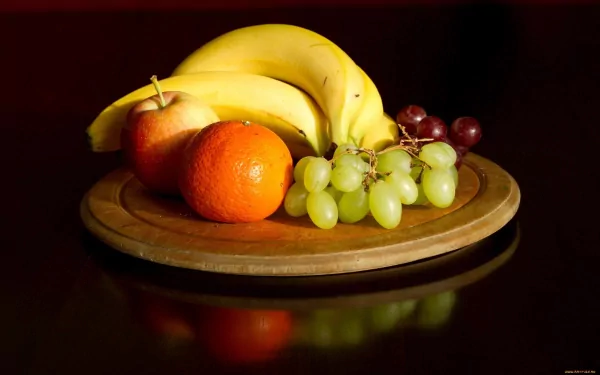 HD PC desktop wallpaper featuring a vibrant assortment of fresh fruit including bananas, apples, an orange, and green and red grapes on a wooden platter.