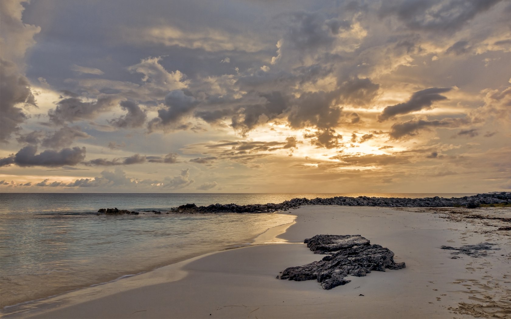 Nature beach HD PC desktop wallpaper and background: tranquil sunset on a sandy shore with rocky outcrops, calm waves and a dramatic, cloud-filled sky.