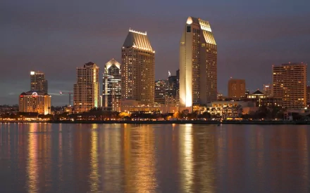 HD desktop wallpaper showing the illuminated man-made skyline of San Diego reflecting on calm waters at dusk.