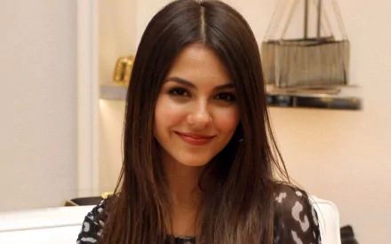 A high-definition wallpaper featuring Victoria Justice, smiling warmly in a stylish setting, showcasing her confident and vibrant personality.