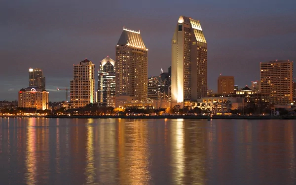 HD desktop wallpaper showing the illuminated man-made skyline of San Diego reflecting on calm waters at dusk.