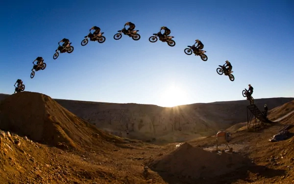 A stunning HD desktop wallpaper featuring a motocross rider performing a sequence of jumps against a beautiful sunset backdrop in a desert landscape.