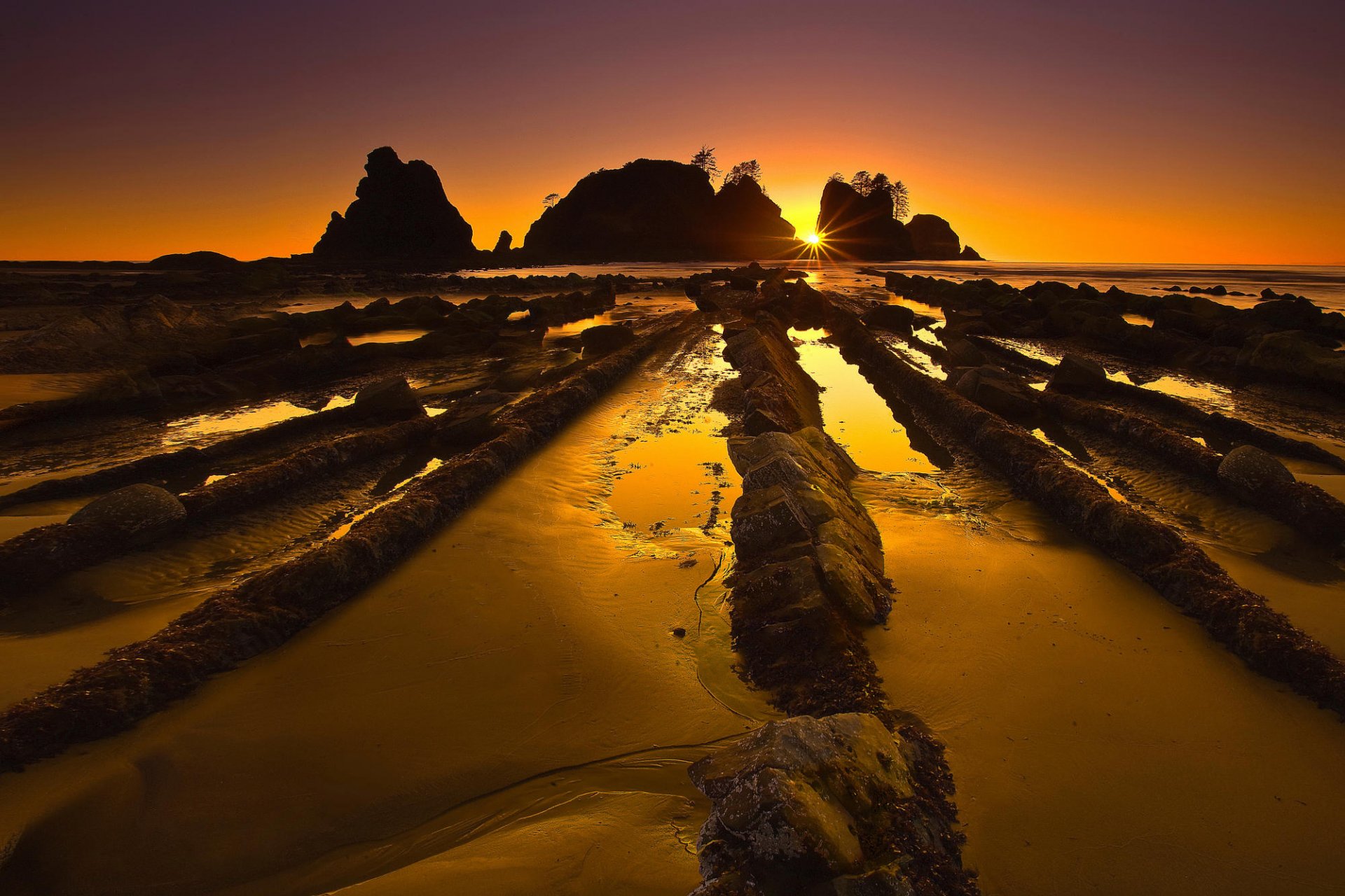 HD PC desktop wallpaper and background: yellow-orange sunset over a rocky beach, tidal channels of water reflecting warm light with silhouetted offshore rocks.