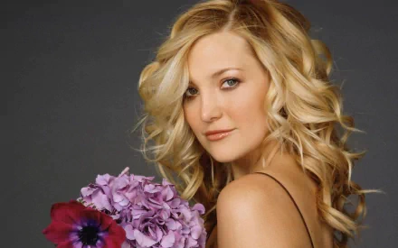 HD PC desktop wallpaper featuring celebrity Kate Hudson with wavy blonde hair holding a bouquet of purple and red flowers against a dark background.