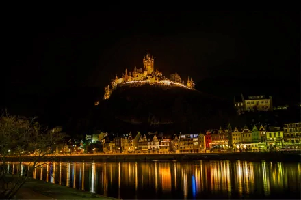 Cochem Castle illuminated at night atop a hill, overlooking the town and river, captured in 4K Ultra HD as a striking man-made architectural landmark.