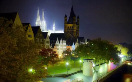 HD PC desktop wallpaper: nighttime view of man-made Cochem Castle and illuminated historic riverside buildings, tree-lined promenade and shimmering water reflections.