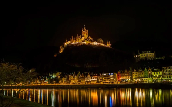 Cochem Castle illuminated at night atop a hill, overlooking the town and river, captured in 4K Ultra HD as a striking man-made architectural landmark.