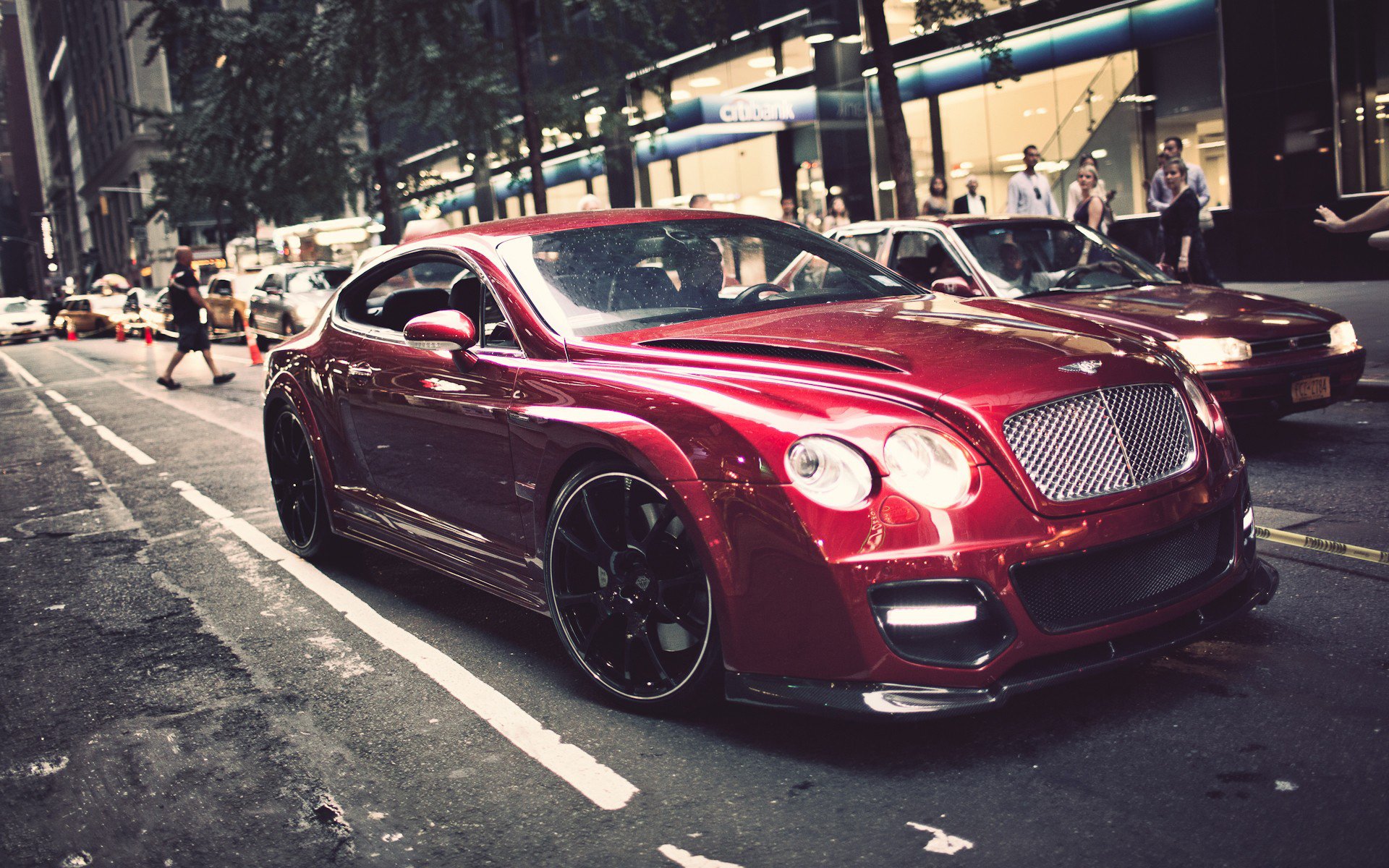 HD PC desktop wallpaper featuring a sleek red Bentley parked on a city street at dusk, highlighting its luxury and sporty design.
