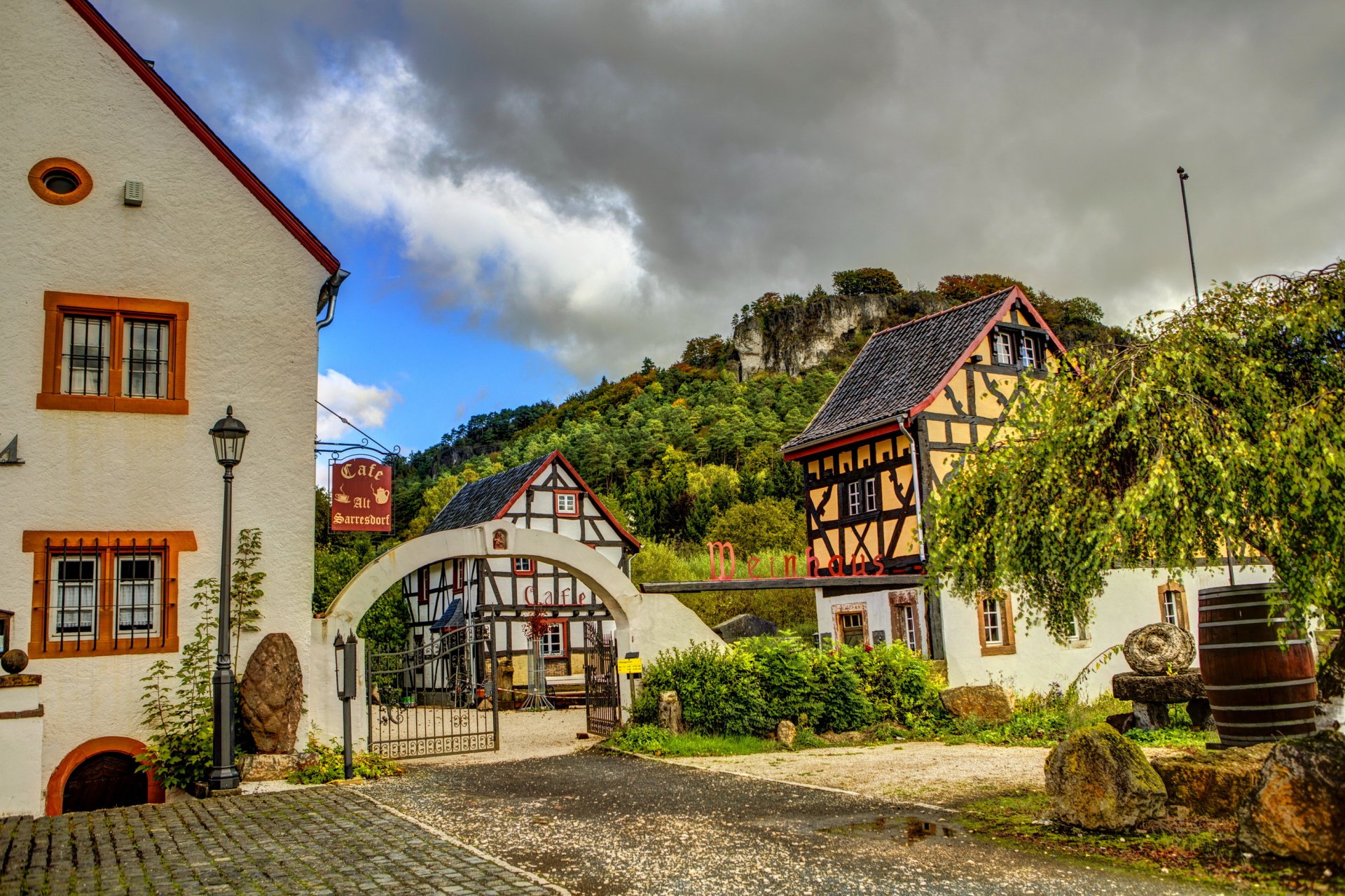 HD desktop wallpaper featuring a charming man-made village with traditional half-timbered houses, cobblestone streets, and lush greenery under a cloudy sky.