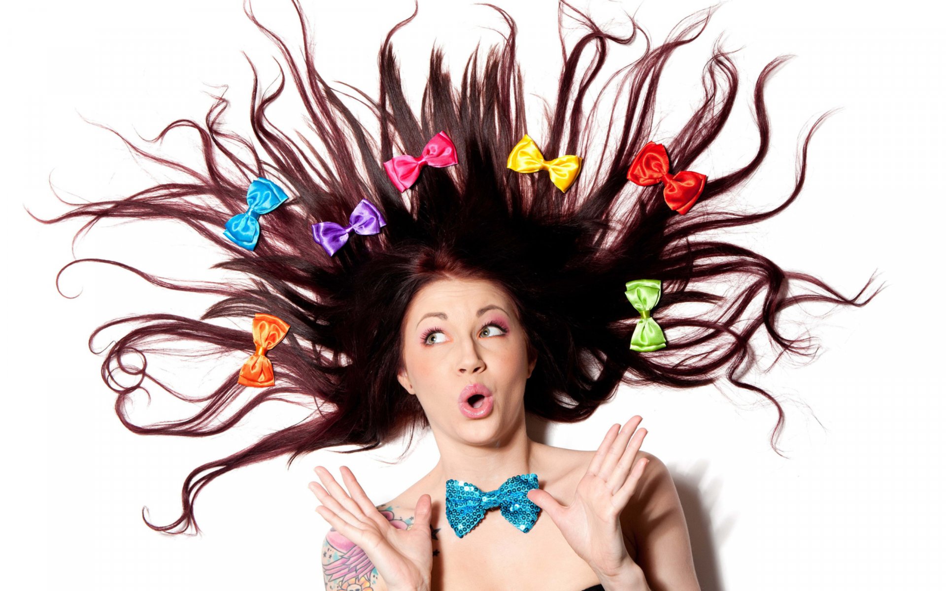 2K Quad HD PC desktop wallpaper of a surprised woman with hair fanned out, colorful bows woven through her strands and a glittery blue bow tie.